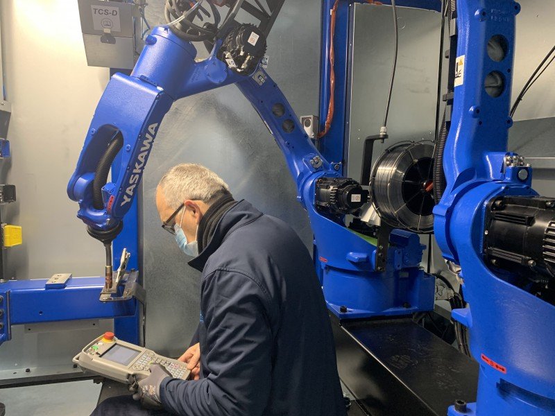 Technician operating blue industrial robotic arm controls