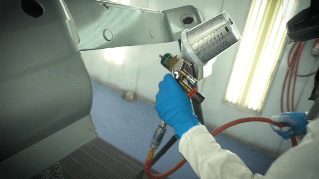 Technician using an HVLP spray gun to apply a uniform coating inside a professional spray booth